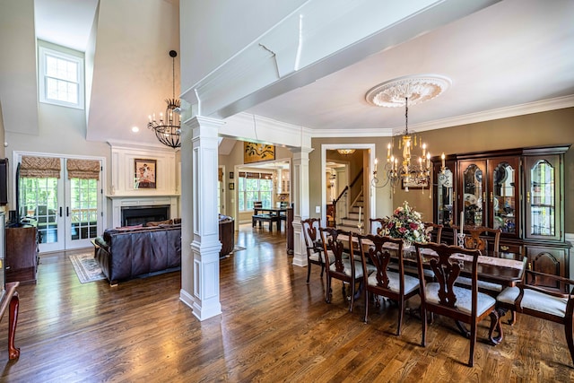 dining area featuring a chandelier, wood finished floors, ornate columns, crown molding, and a towering ceiling