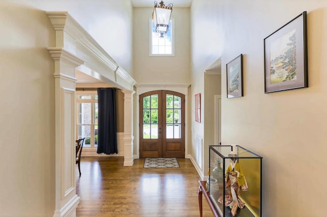 entrance foyer featuring french doors, healthy amount of natural light, wood finished floors, a towering ceiling, and a chandelier