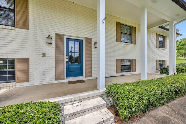 entrance to property featuring a porch and brick siding