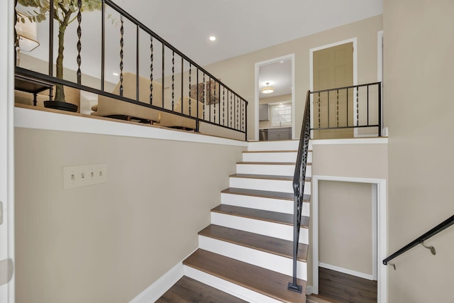 stairway featuring wood finished floors, baseboards, recessed lighting, and a towering ceiling