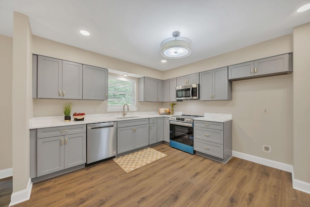 kitchen with stainless steel appliances, gray cabinetry, a sink, baseboards, and wood finished floors