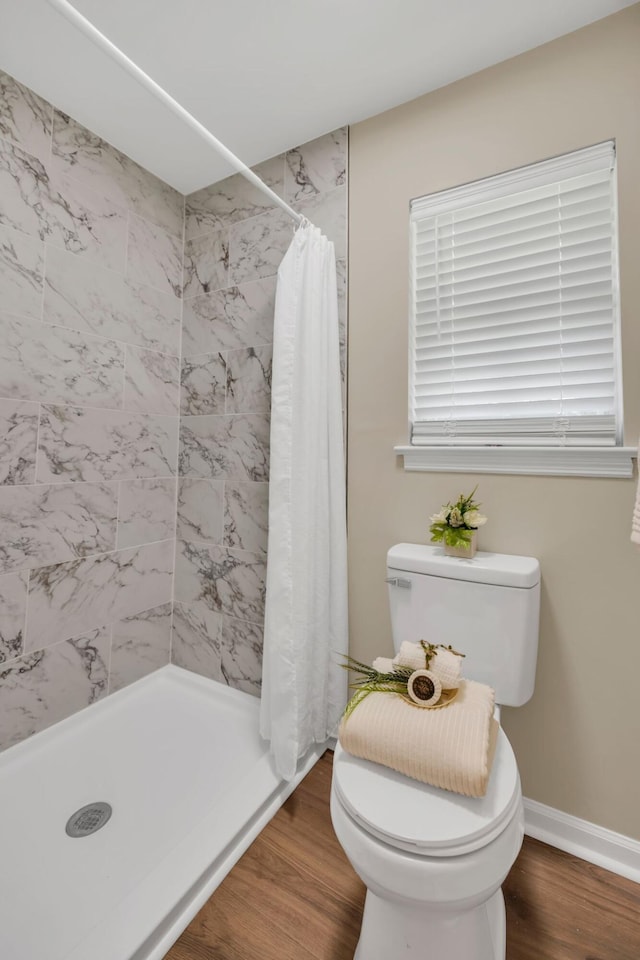 bathroom with toilet, wood finished floors, tiled shower, and baseboards