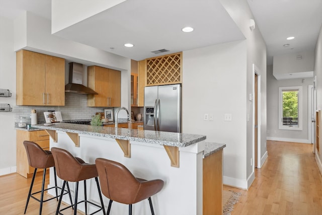 623 Hamilton Ave, Chattanooga, TN 37405 - kitchen featuring stainless steel fridge with ice dispenser, wall chimney range hood, tasteful backsplash, a breakfast bar, and recessed lighting