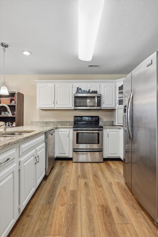 548 Flagstone Dr, Rossville, GA 30741 - kitchen with stainless steel appliances, a sink, light wood-style flooring, white cabinetry, and decorative light fixtures