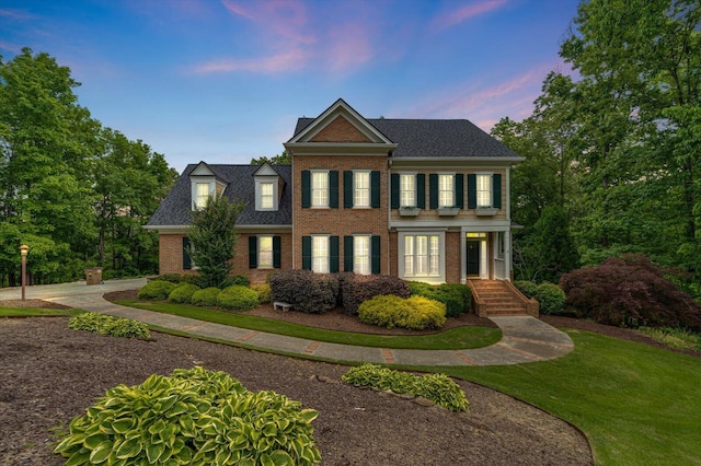 colonial house featuring brick siding, a front lawn, and a chimney