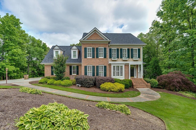 georgian-style home with brick siding, a shingled roof, and a front lawn