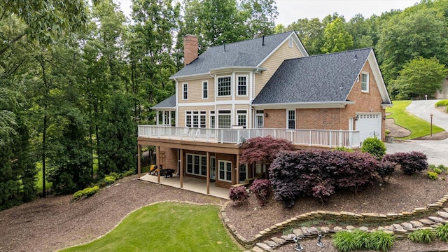 rear view of property with a chimney, a wooden deck, driveway, brick siding, and a patio area