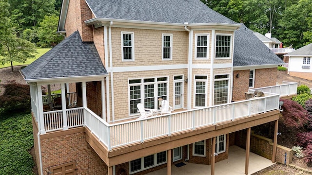 rear view of property with a shingled roof, a patio area, brick siding, and a wooden deck