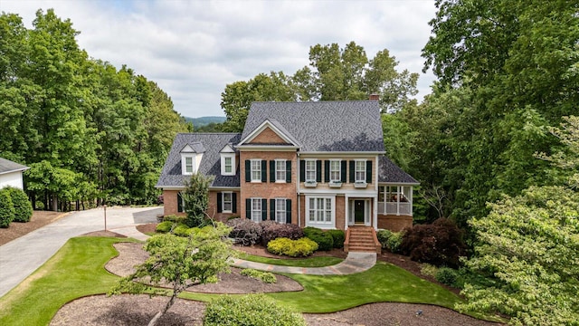 colonial home featuring brick siding, a chimney, and a front lawn