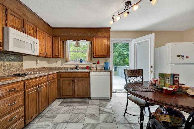 kitchen featuring white appliances, brown cabinetry, a sink, a textured ceiling, and decorative backsplash