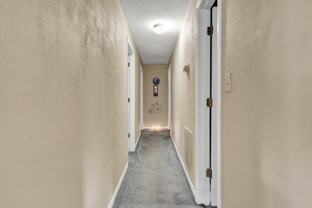 hall featuring carpet flooring, baseboards, and a textured ceiling