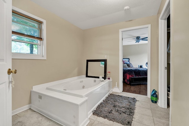 bathroom featuring a tub with jets, a ceiling fan, baseboards, a textured ceiling, and tile patterned floors