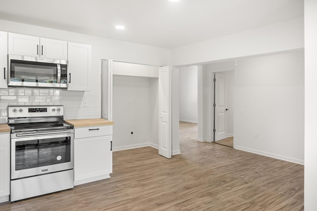 kitchen featuring stainless steel appliances, butcher block countertops, white cabinets, light wood-style floors, and decorative backsplash