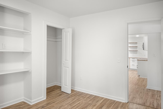 unfurnished bedroom featuring light wood finished floors, baseboards, and a closet