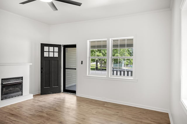 entrance foyer featuring crown molding, a ceiling fan, wood finished floors, baseboards, and a fireplace with raised hearth