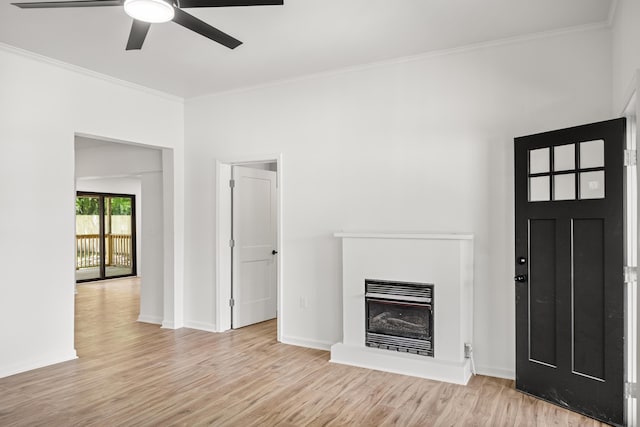 unfurnished living room with ceiling fan, light wood finished floors, ornamental molding, a glass covered fireplace, and baseboards