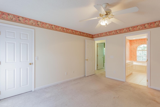 unfurnished bedroom with light colored carpet, baseboards, ensuite bathroom, and ceiling fan
