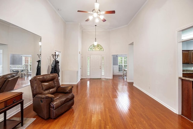 foyer featuring a ceiling fan, wood finished floors, crown molding, a high ceiling, and baseboards