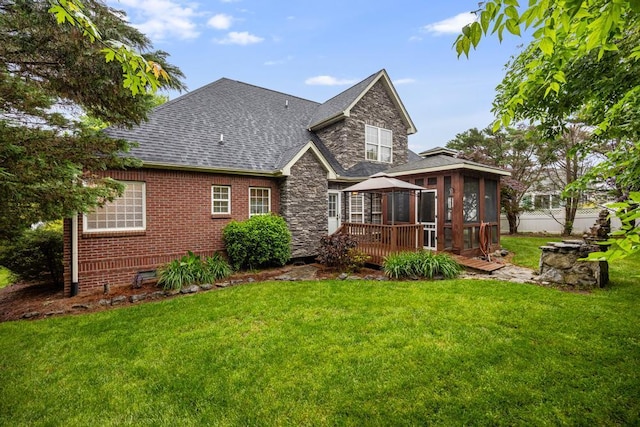 rear view of house featuring a sunroom, a shingled roof, a deck, a gazebo, and brick siding