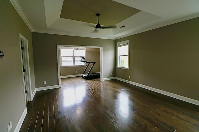 spare room with a tray ceiling, a ceiling fan, ornamental molding, dark wood-style floors, and baseboards