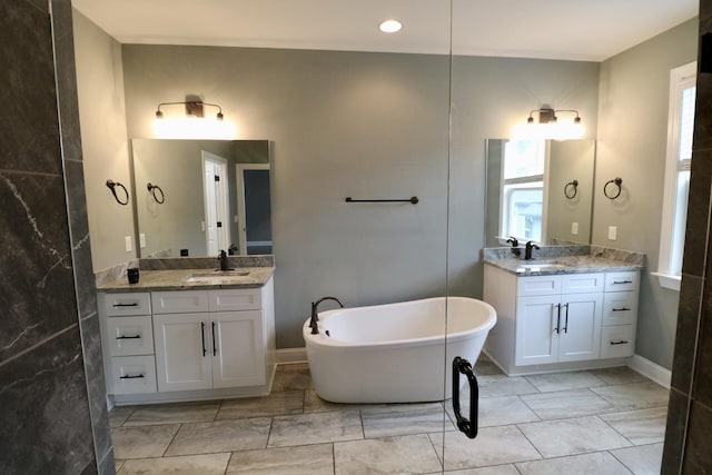 full bath featuring marble look tiles, a soaking tub, and two vanities