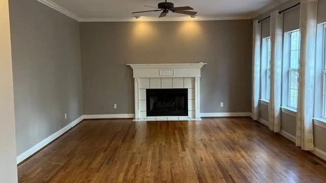 unfurnished living room featuring a ceiling fan, wood finished floors, baseboards, a tile fireplace, and crown molding