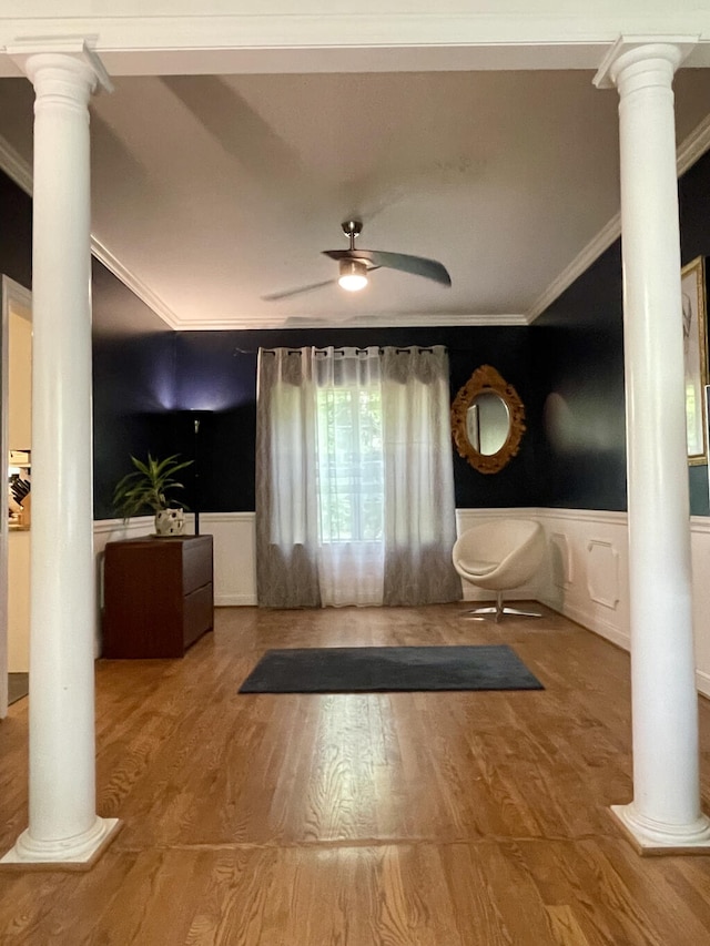 foyer with decorative columns, ornamental molding, ceiling fan, a wainscoted wall, and wood finished floors