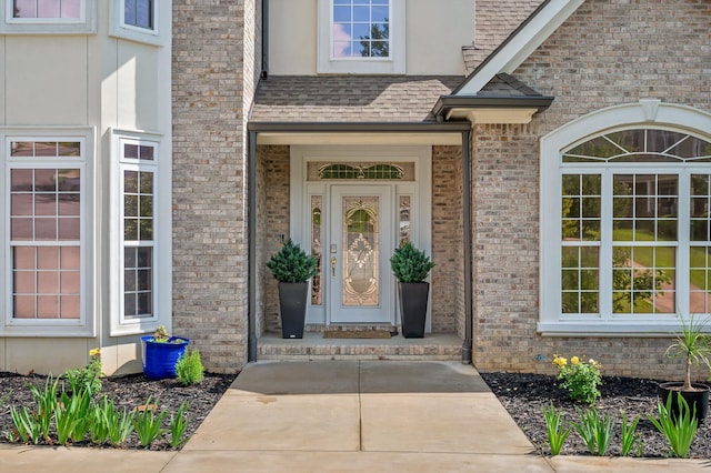 entrance to property with roof with shingles and brick siding