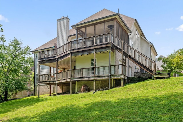 rear view of house featuring a chimney, a deck, a sunroom, a lawn, and a shingled roof