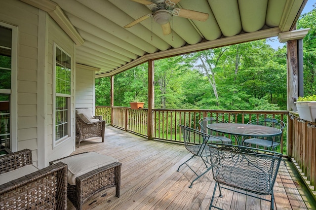 wooden terrace with ceiling fan, outdoor dining space, and view of scattered trees