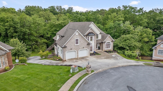 traditional-style house with concrete driveway, an attached garage, a front lawn, roof with shingles, and a forest view