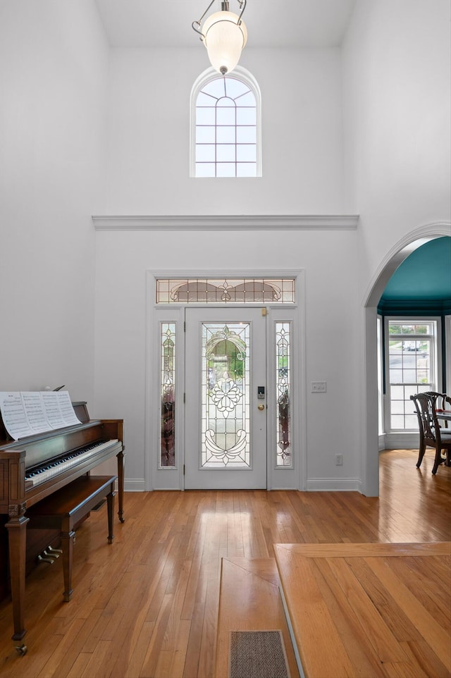 entrance foyer featuring arched walkways, a high ceiling, hardwood / wood-style floors, and baseboards