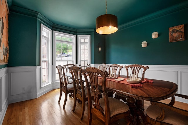 dining area featuring a decorative wall, wainscoting, light wood finished floors, and ornamental molding