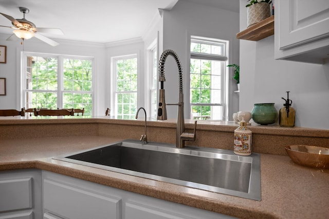 kitchen featuring a sink, plenty of natural light, white cabinetry, a ceiling fan, and ornamental molding