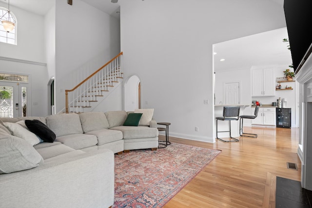 living area featuring a high ceiling, stairs, light wood-type flooring, arched walkways, and baseboards