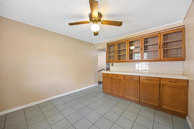 3502 Oak Ridge Dr, Chattanooga, TN 37415 - kitchen with brown cabinetry, ceiling fan, light tile patterned flooring, glass insert cabinets, and a textured ceiling