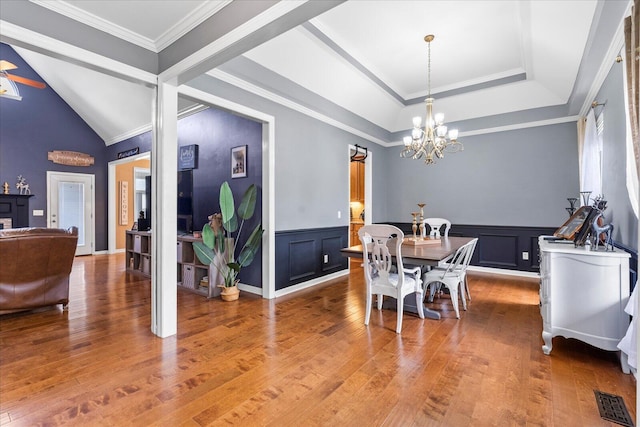 dining area featuring a chandelier, wood finished floors, a wainscoted wall, a decorative wall, and vaulted ceiling
