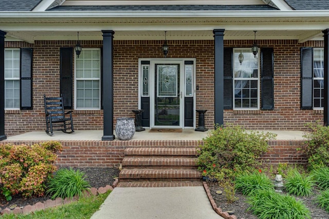 property entrance with brick siding, covered porch, and roof with shingles