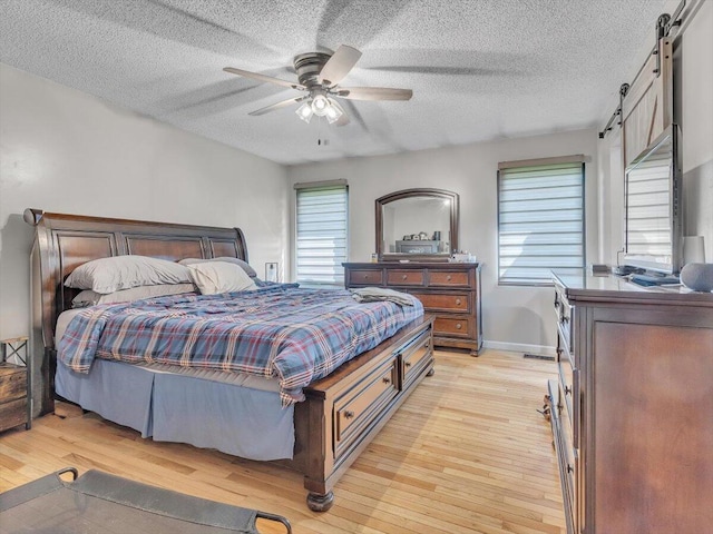 123 Paddle Wheel Ct, Cohutta, GA 30710 - bedroom with a barn door, light wood-type flooring, a textured ceiling, ceiling fan, and baseboards