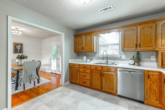 kitchen with stainless steel dishwasher, a sink, light countertops, brown cabinetry, and a textured ceiling