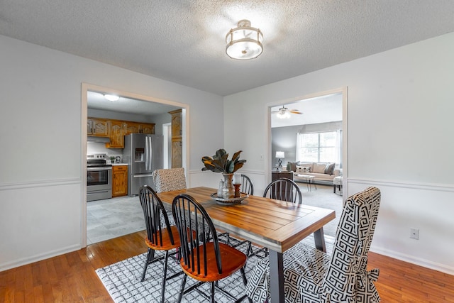 dining room featuring a textured ceiling, light wood-style floors, baseboards, and ceiling fan
