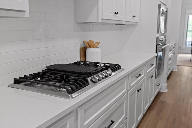kitchen featuring stainless steel appliances, white cabinets, light countertops, and backsplash