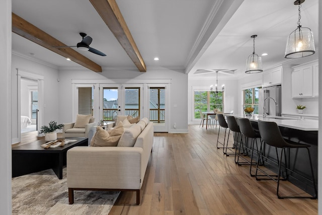 living room with light wood finished floors, baseboards, a chandelier, beamed ceiling, and ornamental molding