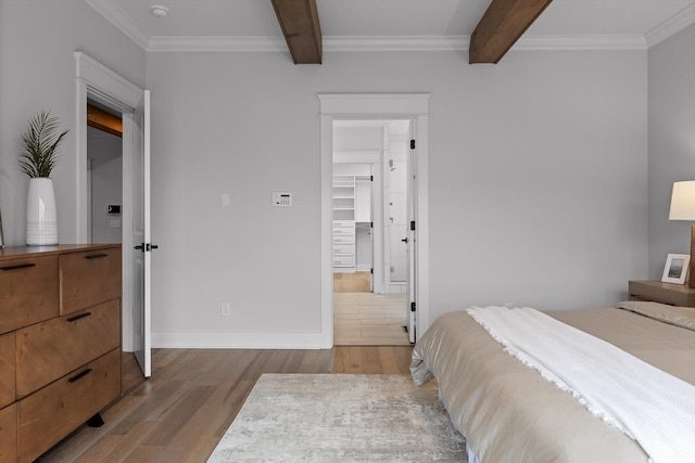 bedroom featuring wood finished floors, beam ceiling, ornamental molding, a spacious closet, and baseboards