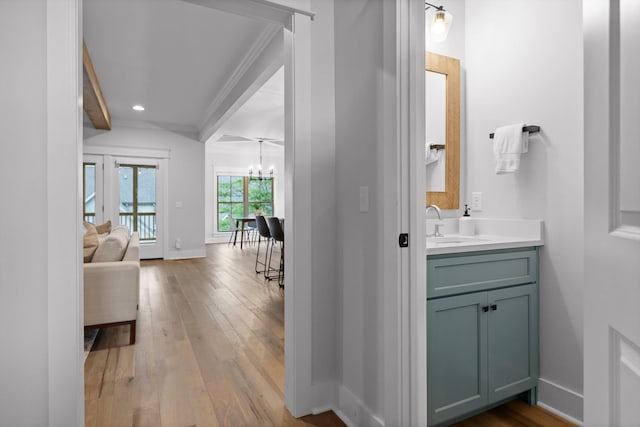 bathroom with wood finished floors, a chandelier, baseboards, crown molding, and vanity
