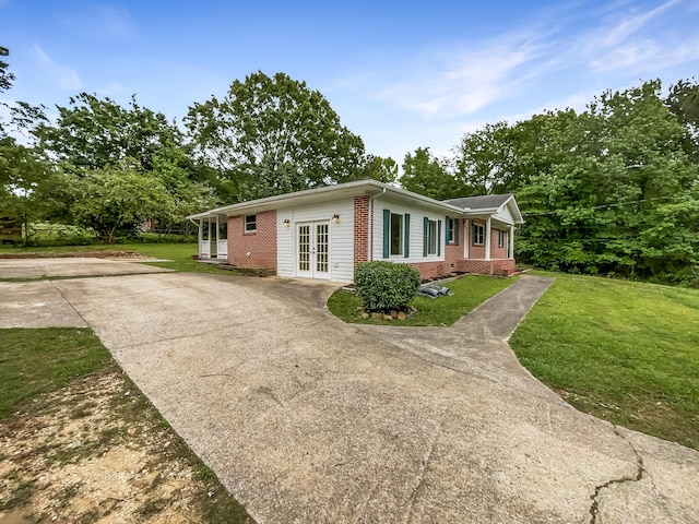 view of property exterior featuring french doors, brick siding, driveway, and a yard