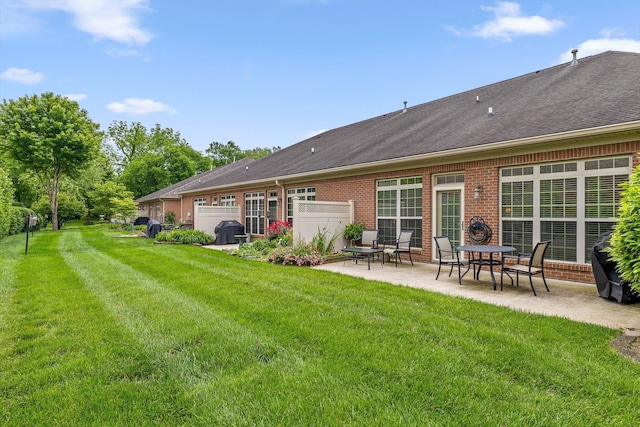 rear view of property with a patio area, brick siding, a lawn, and a shingled roof