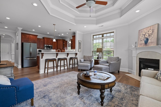 living area with arched walkways, a ceiling fan, ornamental molding, recessed lighting, and wood finished floors