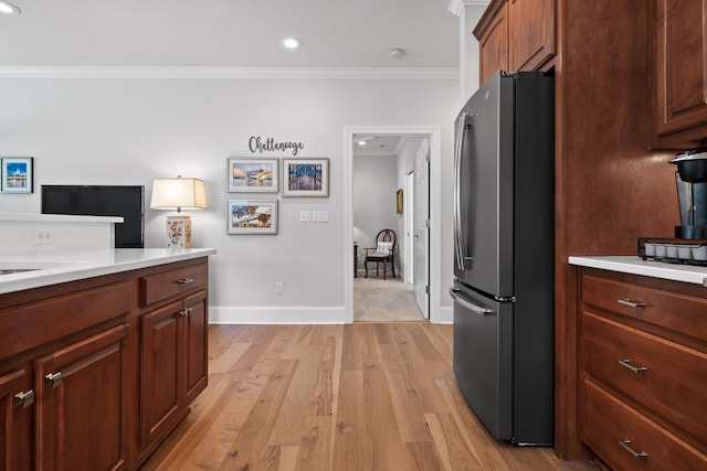kitchen with freestanding refrigerator, crown molding, light wood-type flooring, light countertops, and baseboards