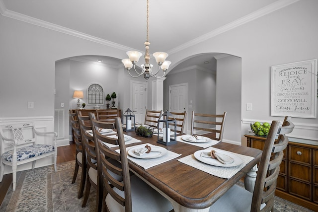 dining room featuring arched walkways, wood finished floors, ornamental molding, a chandelier, and wainscoting